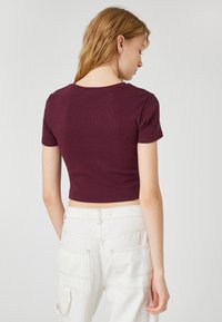Bordeaux crop top med korte ærmer, ribbet tekstur og rund halsudskæring, parret med hvide højtaljede cargo bukser.