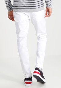 Vita denimjeans med smal passform, med bakfickor, kombinerade med svartvita sneakers med röda detaljer. Randig grå långärmad skjorta.