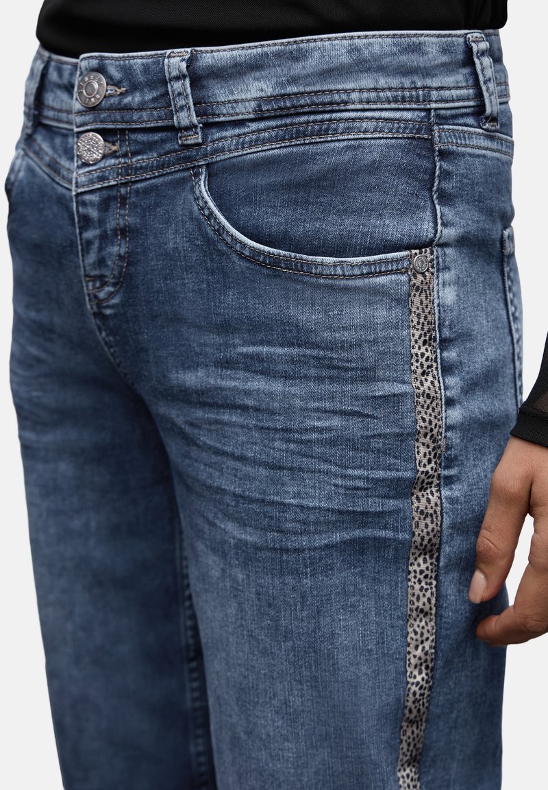Pantalones vaqueros de mezclilla en lavado azul medio con un acento de estampado de leopardo a lo largo del costado, con dos botones metálicos en la cintura y un diseño clásico de cinco bolsillos.