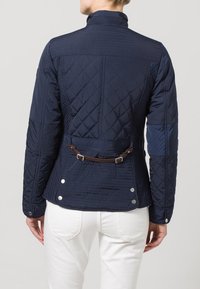 Granatowa pikowana kurtka z wysokim kołnierzem, z kontrastującym niebieskim materiałem, brązowym paskiem jako akcentem oraz srebrnymi zatrzaskami przy dole.