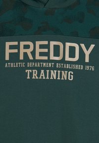 Felpa verde con cappuccio e design testurizzato, con le parole "FREDDY" e "TRAINING" in grandi caratteri chiari. Realizzata in tessuto morbido.