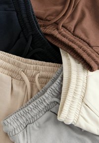 Cotton sweatpants in brown, black, beige, and gray; features an elastic waistband with drawstrings and ribbed detailing at the edges.