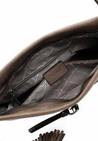 Interno di una borsa a tracolla in pelle marrone con tasca con zip e due comparti; foderato con un tessuto a motivo geometrico in grigio e bianco.