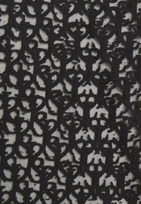 Tela de encaje negro con un intrincado diseño de recortes abstractos y patrones abiertos sobre un fondo beige, que muestra textura y detalle.