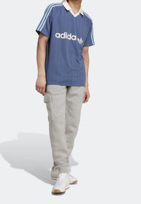 Blå kortärmad polo med vertikala ränder, vit krage och Adidas-logotyp, tillsammans med ljusgrå sweatpants och vita sneakers.