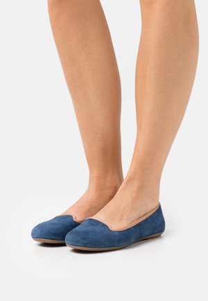 Des ballerines en suède bleu avec un bout rond et une découpe basse, ornées d'accents beiges le long du bord, reposant sur une semelle plate.