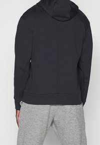 Sudadera gris oscuro con capucha, con una textura suave y un corte relajado, combinada con pantalones de chándal gris claro. Sin logotipos ni patrones visibles.