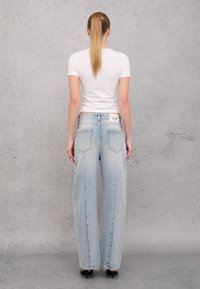 Light blue, wide-leg denim jeans with a frayed hem, featuring back pockets and a white label on the waistband. Paired with a fitted white t-shirt.