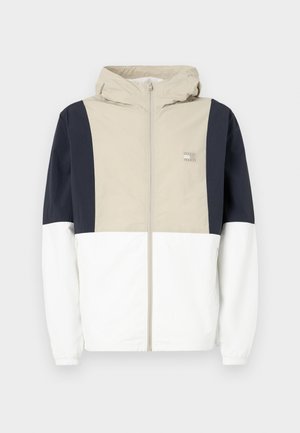 Färgblockerad jacka med en beige övre del, marinblå ärmar och vit nedre del. Inkluderar en huva och främre dragkedja. Lätt material.