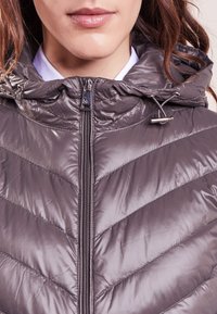 Lätt pufferjacka i mörkgrått med en chevron-quiltad mönster, dragkedjestängning och justerbar huva. Slät, glänsande yta.