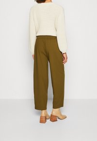 Pull en maille crème avec des manches larges, associé à un pantalon à jambes larges olive et à des chaussures à talons blocs beiges texturées avec des bases en bois.