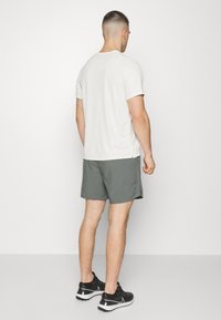 Herren ljusgrå kortärmad skjorta med rund halsringning, tillsammans med mörkgröna shorts och svarta träningsskor. Enkel, funktionell design.