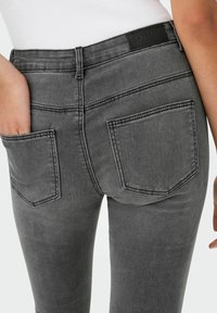 Harmaat farkut, joissa on keskikorkea vyötärö, takataskut ja erottuva ompelu. Materiaali näyttää pehmeältä ja klassiselta. Musta vyötärövyön etiketti näkyvissä.