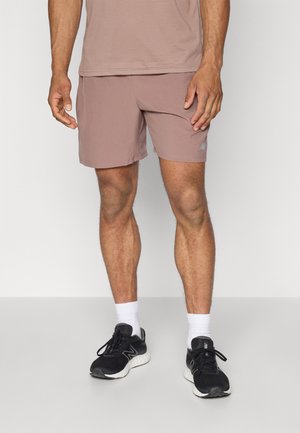 Îmbrăcăminte sportivă pentru bărbați, compusă din pantaloni scurți bej deschis cu un logo, asortați cu adidași negri și șosete albe sport. Design simplu, țesătură netedă.