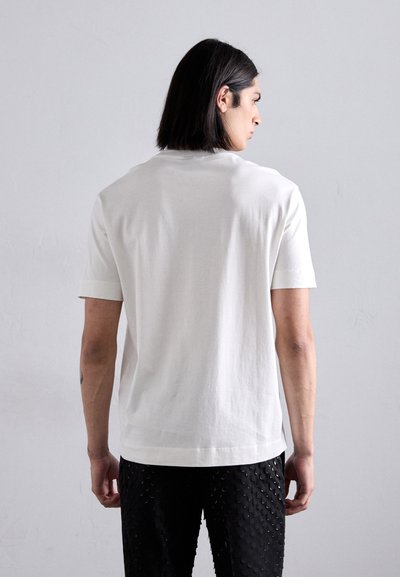 White cotton t-shirt with a round neckline and short sleeves, paired with black textured trousers featuring raised circular patterns.