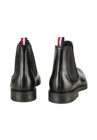 Crne kožne Chelsea čizme s elastičnim bočnim panelima, okruglim vrhovima i kontrastnim crvenim, bijelim i plavim tabom na peti. Glatka tekstura i minimalistički dizajn.