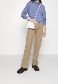 Světle fialová mikina s kapucí a přední kapesní, béžové manšestrové široké kalhoty a černé robustní boty na platformě. Bílá kabelka přes tělo.