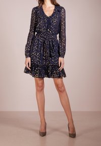 Marinblå klänning med gyllene prickar, volangkrage, långa ärmar, dragsko i midjan och flerlagad nederdel, tillverkad i lätt, genomskinlig tyg.