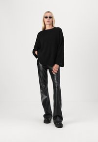 Svart oversized genser med ribbestruktur i kanten, kombinert med blanke svarte bukser i faux skinn med vidde. Modellen har på seg smale svarte solbriller.