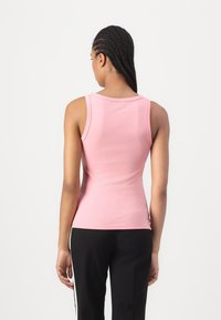 Haut sans manches rose clair en matière extensible, avec un col rond et un design ajusté, associé à un pantalon noir avec des accents blancs.