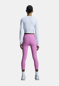 Weißes langärmliges Crop-Top in Kombination mit rosa High-Waisted-Leggings. Material aus Baumwollmischung, figurbetontes Design und nahtlose Details an der Taille.