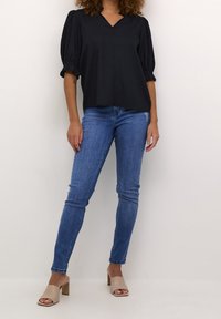 Blouse noire à manches courtes avec encolure en V, associée à un jean bleu ajusté et des mules à talons carrés ouvertes beiges. Tissu lisse, coupe décontractée.