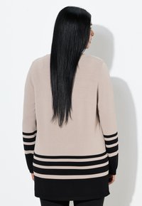 Pletený top s dlouhými rukávy v béžové a černé barvě, se zvýrazněnými horizontálními pruhy na lemu a rukávech, s volným střihem a jemnou texturou.