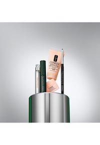 Clinique-Produkte, die auf einem metallischen Behälter präsentiert werden: eine silberne Sprühflasche, ein grüner Mascara-Stift, eine pfirsichfarbene Feuchtigkeitscreme und ein schwarzer Eyeliner.