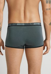 Kalsonger för män i mörkgrått tyg med en slät textur, som har en svart midja med branding och en kroppsnära passform.