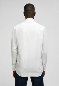Witte lange mouwen shirt met een spreidkraag, voorzien van knoopmanchetten en een gebogen zoom. Glad textuur en eenvoudig ontwerp.