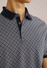 Polokošile s krátkým rukávem v námořnické modři se geometrickým vzorem, s límečkem a dvouknoflíkovým zapínáním. Měkká tkanina s kontrastním límečkem.