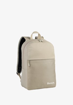 Beige backpack made of fabric with a honeycomb texture. Features a front zip pocket and padded black mesh straps. 'Bench.' logo at the front.