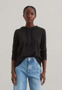 Zwarte hoodie met lange mouwen en een relaxed fit, gecombineerd met lichtblauwe high-waisted jeans met vervaagde details.