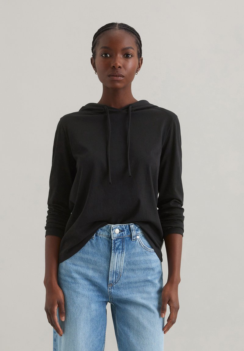 Zwarte hoodie met lange mouwen en een relaxed fit, gecombineerd met lichtblauwe high-waisted jeans met vervaagde details.