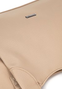 Beige leren handtas met een gladde textuur, voorzien van een subtiel nerfpatroon en een metallic logo plaat. Eenvoudig, elegant ontwerp.