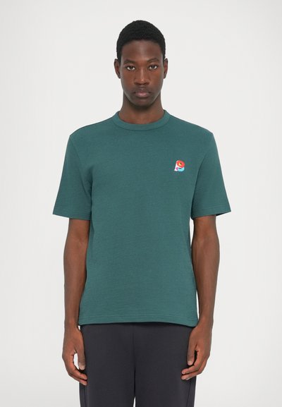 Camiseta de manga corta verde oscuro hecha de tejido texturizado, con un pequeño logo multicolor en la parte izquierda del pecho.