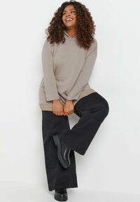 Huppari vaaleassa beigeissä sävyissä, jossa on etutasku, pitkät hihat ja ribbineule. Kirjava kankaasta. Yhdistetty mustiin leveälahkeisiin housuihin ja mustiin nilkkureihin.