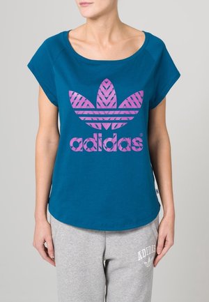 Teal cotton t-shirt with a wide neckline and short sleeves, featuring a large pink striped Adidas logo prominently displayed on the front.
