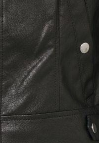 Giubbotto di pelle nero con superficie testurizzata, caratterizzato da cuciture in evidenza e chiusure a pressione argentate sulle tasche frontali.