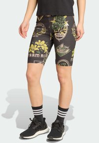 Bermudas de bicicleta pretas com padrões florais e gráficos, feitas de material elástico. Usadas com sapatilhas atléticas pretas e meias às riscas.