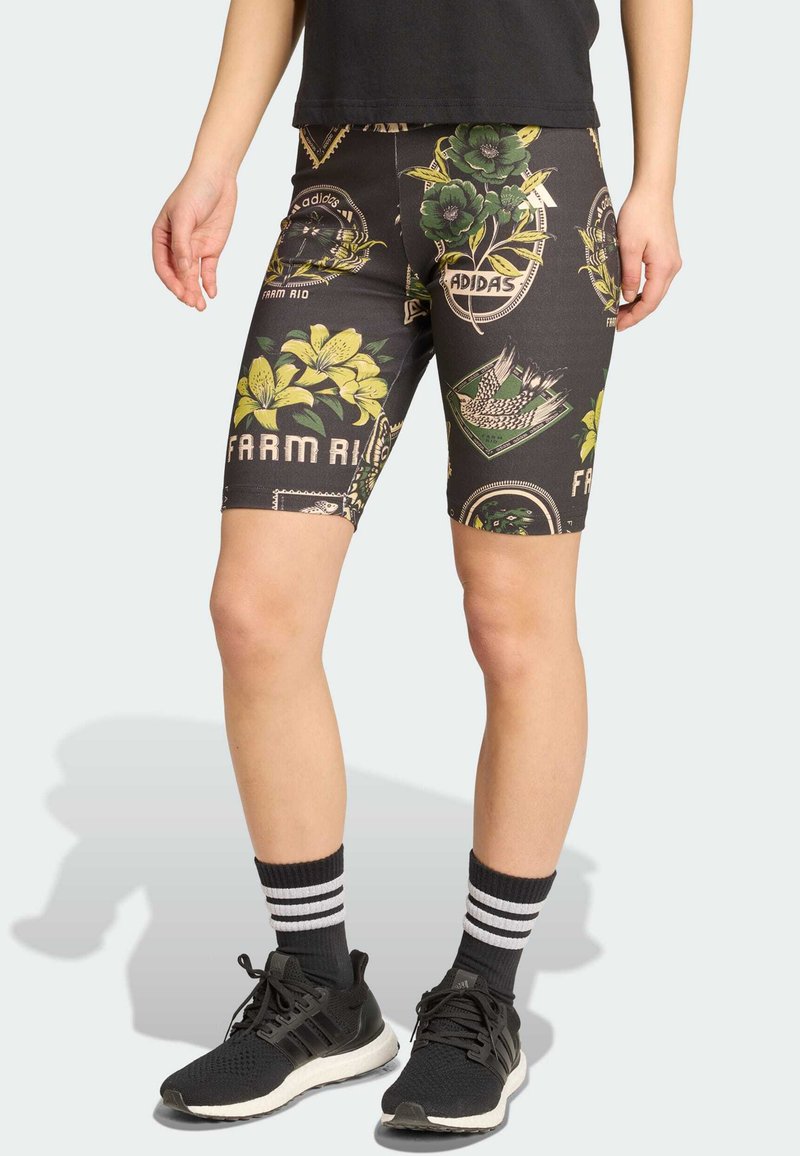 Bermudas de bicicleta pretas com padrões florais e gráficos, feitas de material elástico. Usadas com sapatilhas atléticas pretas e meias às riscas.