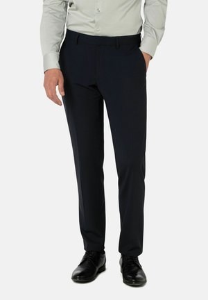 Marineblaue maßgeschneiderte Hose mit flachem Bund, seitlichen Taschen und glatter Stoffoberfläche, kombiniert mit schwarzen Oxford-Schuhen und einem hellgrauen Hemd.
