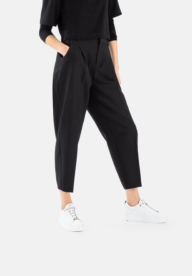 Black tailored trousers with pleats, featuring side pockets and a cropped ankle length, paired with white sneakers. Smooth texture.