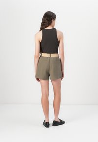 Juodas marškinėlis be rankovių su laisvu siluetu, derinamas su alyvmedžių spalvos šortais, turinčiais diržo juostą, nugaros kišenes ir lygiu paviršiumi.