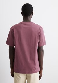 Camiseta de algodón en color rosa viejo, de manga corta y cuello redondo, con un corte relajado y sin marcas ni patrones visibles.