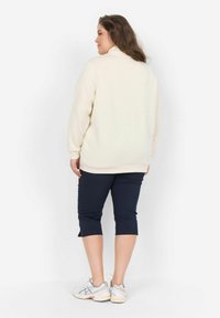 Suéter de color beige claro con cuello alto, combinado con pantalones capri azul marino. El suéter presenta mangas largas y un corte holgado, confeccionado en un material suave.