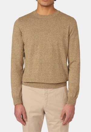 Beige stickad tröja med långa ärmar och rund halsringning. Har en texturerad yta och åtsittande fåll. Matchad med ljusa byxor.