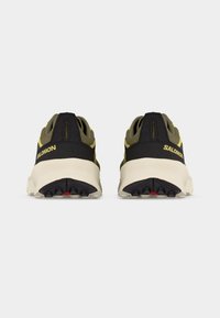 Ζευγάρι αθλητικά παπούτσια Salomon σε ελιά και μαύρο με μπεζ σόλες, εμφανιζόμενα από πίσω σε λευκό φόντο.