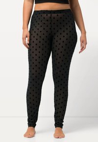 Schwarze Leggings mit Punkten aus durchsichtigem Material, mit einem figurbetonten Design und elastischem Bund. Die Hautfarbe ist durch den Stoff hindurch sichtbar.