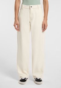 Pantaloni a gamba larga color crema realizzati in materiale morbido, con chiusura a bottone e tasche frontali, abbinati a sneakers nere.